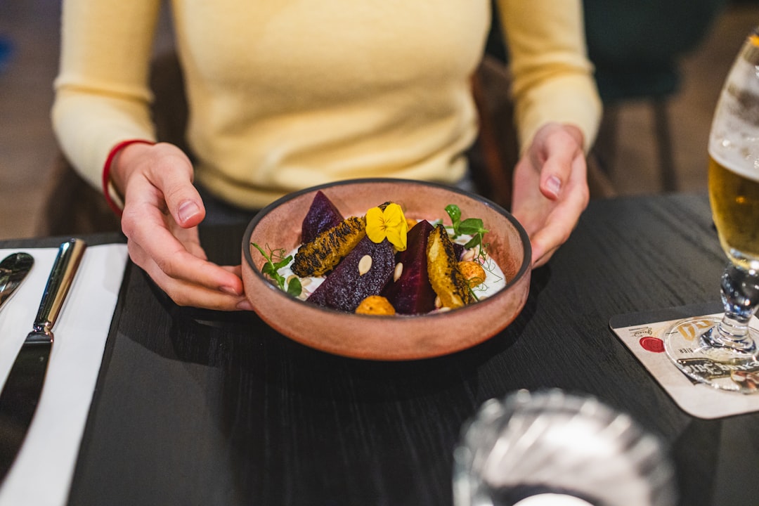 Hands holding a bowl of roasted vegetables in sauce.